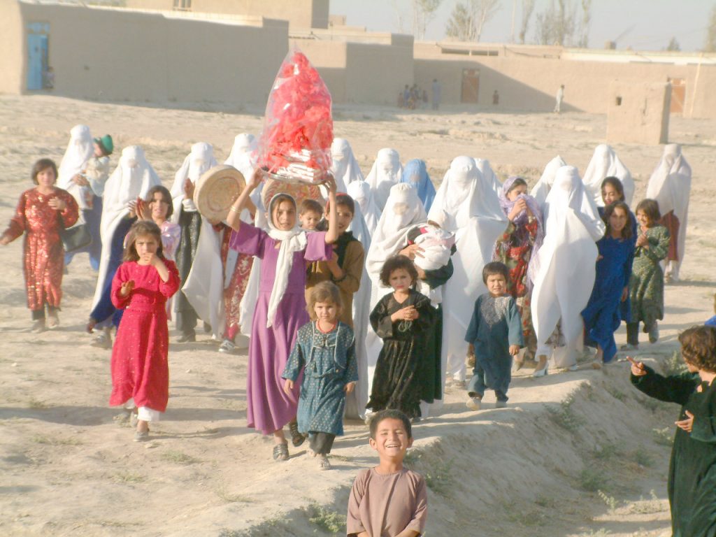 Grupo de crianças e mulheres em vestes coloridas caminhando numa paisagem árida.
