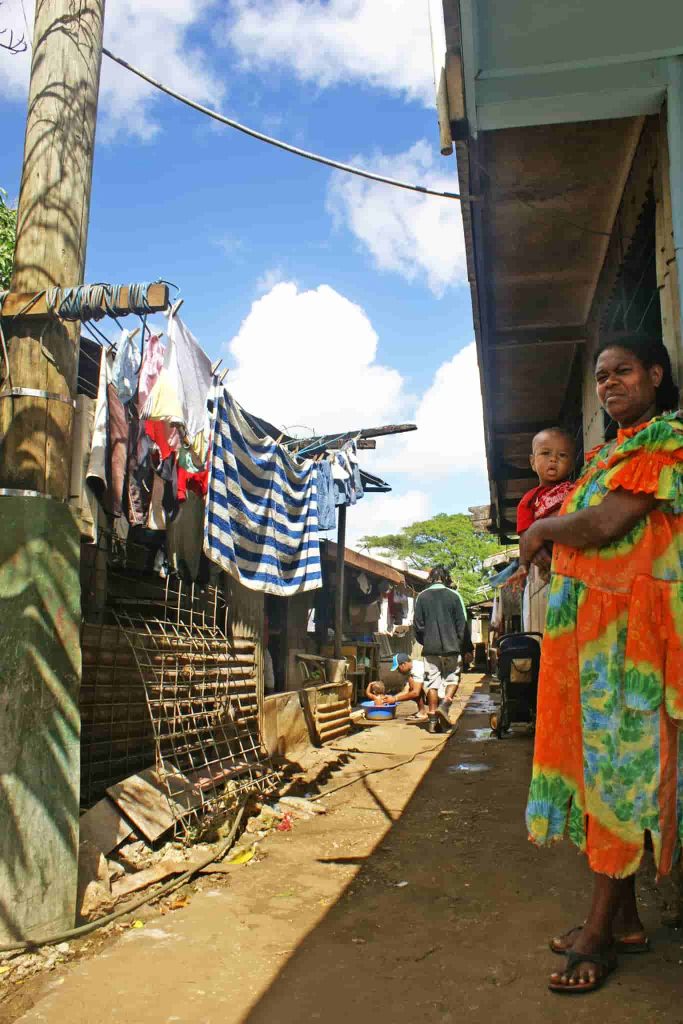Rua de uma comunidade com roupas estendidas e uma mulher com uma criança ao colo.
