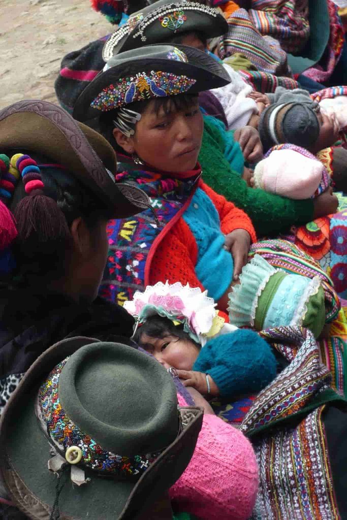 Mulheres indígenas com trajes coloridos e crianças em mantas.