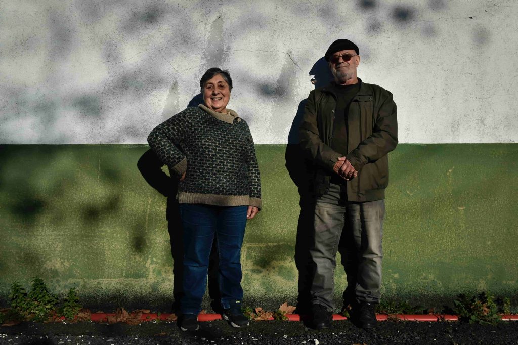 Homem e mulher sorridentes em frente a uma parede verde e branca.
