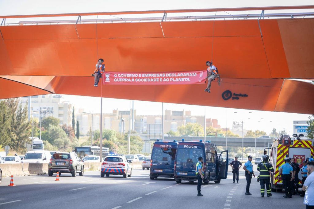 Ativistas pendurados em ponte com faixa de protesto.
