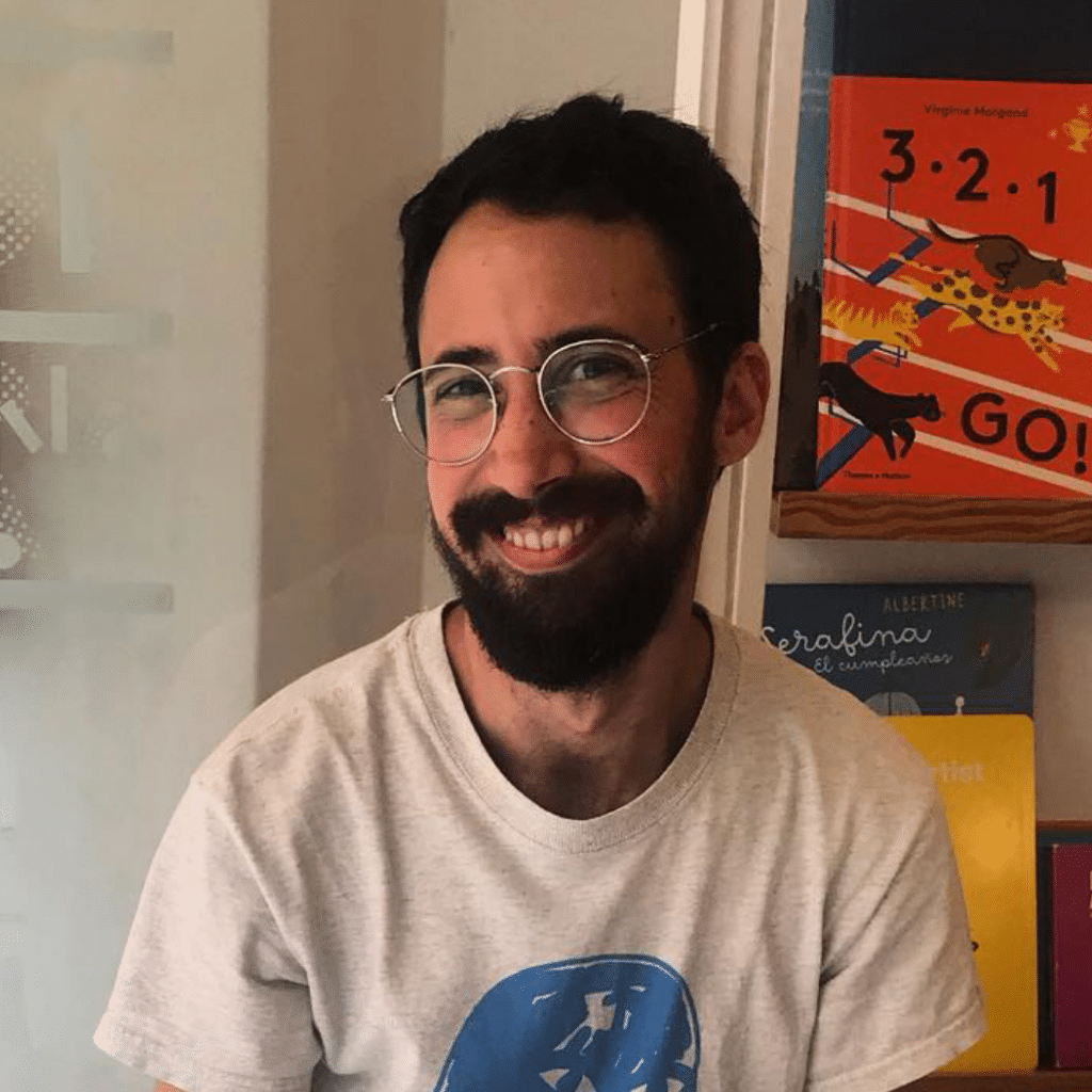 Um homem sorridente com óculos em frente a prateleiras de livros.