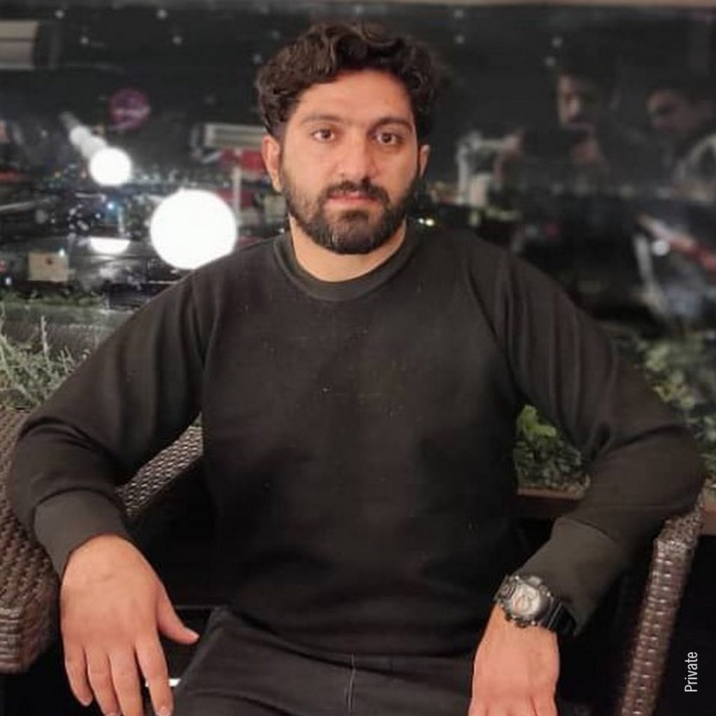 Homem de barba sentado em cadeira, com suéter preto.