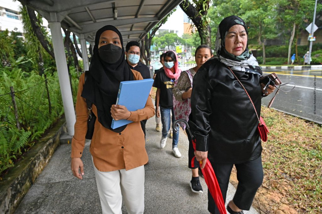 Grupo de mulheres a caminhar sob um abrigo, algumas com máscaras e dois carregando pastas.