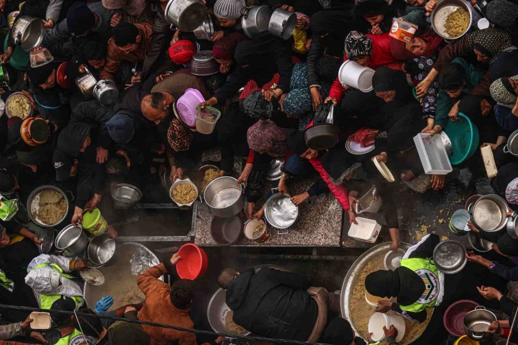 Os palestinianos recebem rações alimentares num ponto de doação num campo para deslocados internos em Rafah, no sul da Faixa de Gaza, a 2 de fevereiro de 2024, enquanto os combates continuam entre Israel e o grupo palestiniano Hamas. Foto de SAID KHATIB/AFP via Getty Images.