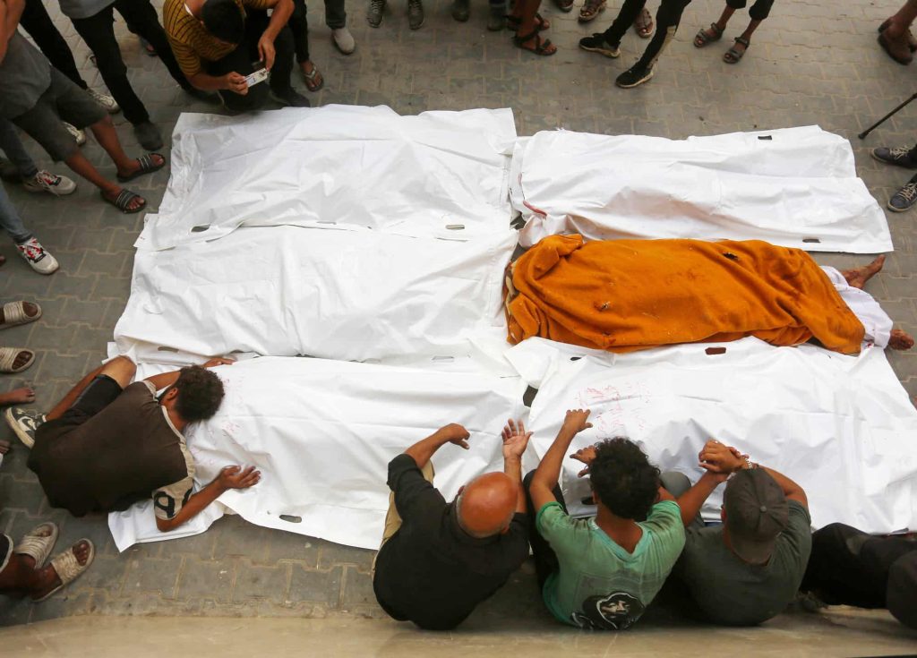 Familiares dos falecidos choram junto aos seus corpos envoltos em mortalhas, depois de as vítimas de um ataque israelita à casa de Faram terem sido levadas para o Hospital Al Awda, em Jabalia, Gaza, a 20 de setembro de 2024. (Fotografia de Ashraf Amra/Anadolu via Getty Images)