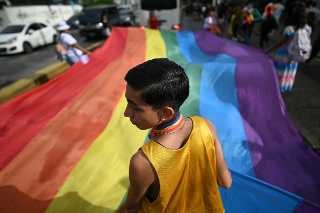 Apoiantes da comunidade LGBT+ seguram uma grande bandeira arco-íris enquanto participam na Marcha do Orgulho em San Salvador, a 29 de junho de 2024. Foto de MARVIN RECINOS/AFP via Getty Images.