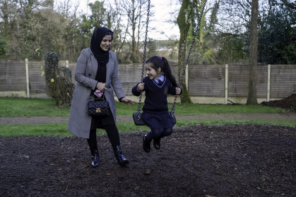 Fawzyah Sarwary empurra a filha num baloiço num parque local. Fawzyah, o marido Fawad Borha e as duas filhas reinstalaram-se em Naas, na Irlanda, vindos do Afeganistão, com a ajuda de um grupo de apoio local (a 16 de janeiro de 2025). Foto © Amnesty International